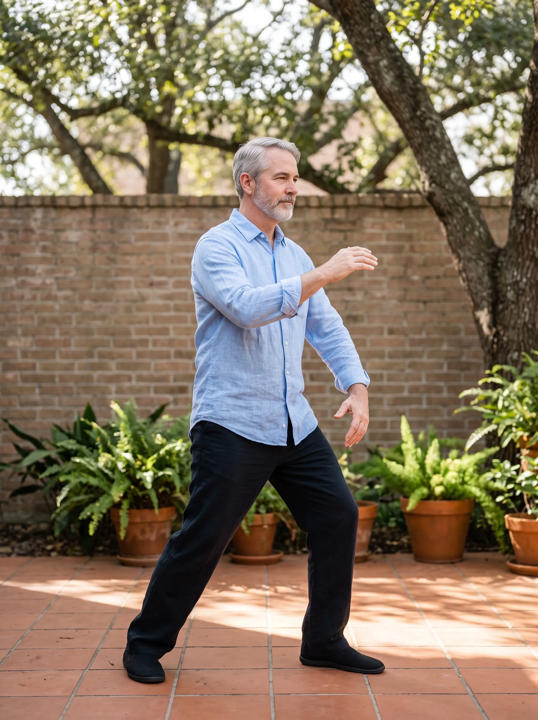 A man in his mid-fifties moving through a slow, balanced tai chi stance on a sunlit Montrose courtyard patio, calm and steady.