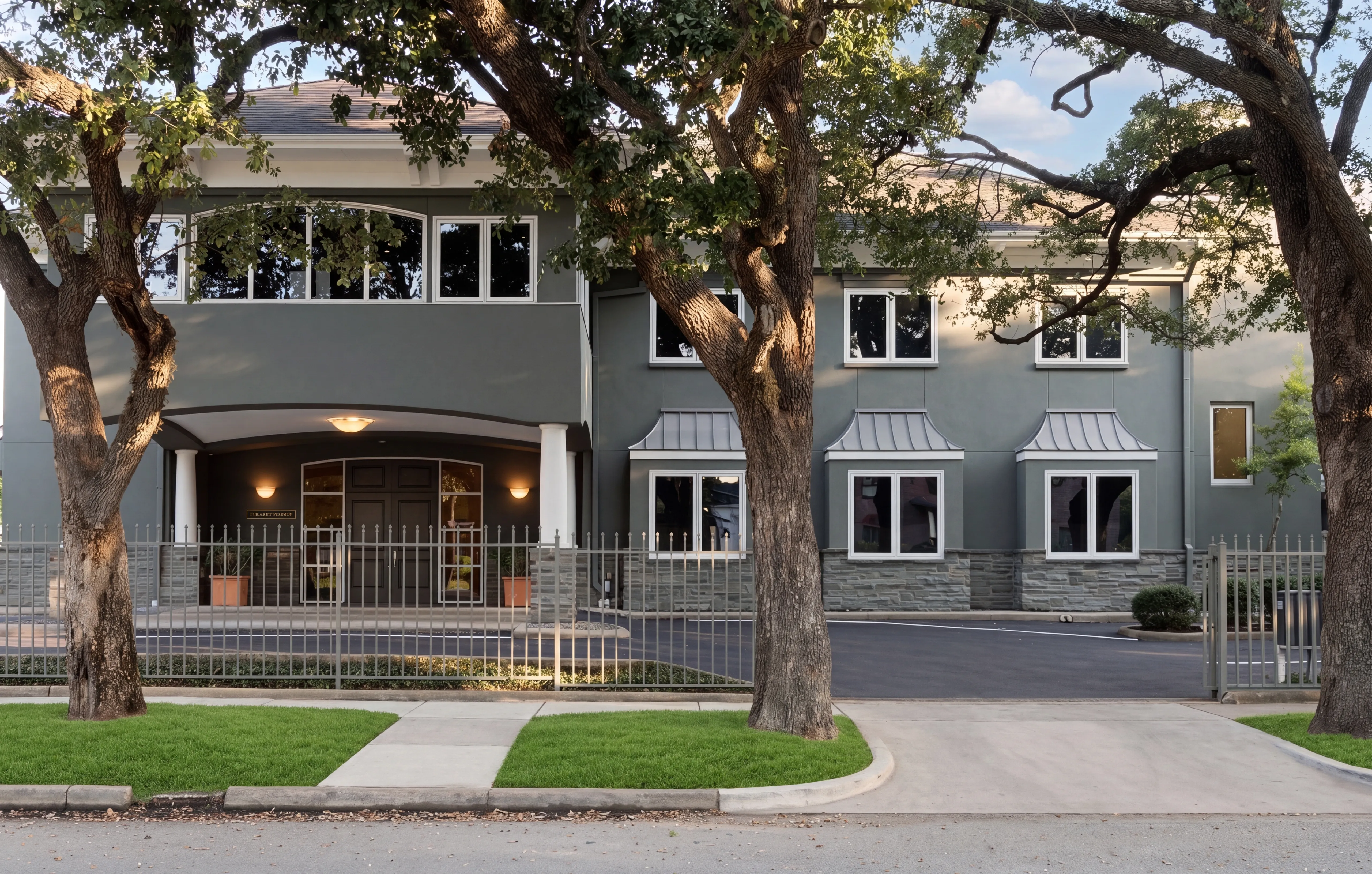 The Lovett Center exterior at 900 Lovett Boulevard: a two-story stucco building with arched portico, set back from the street under mature oaks in Montrose.
