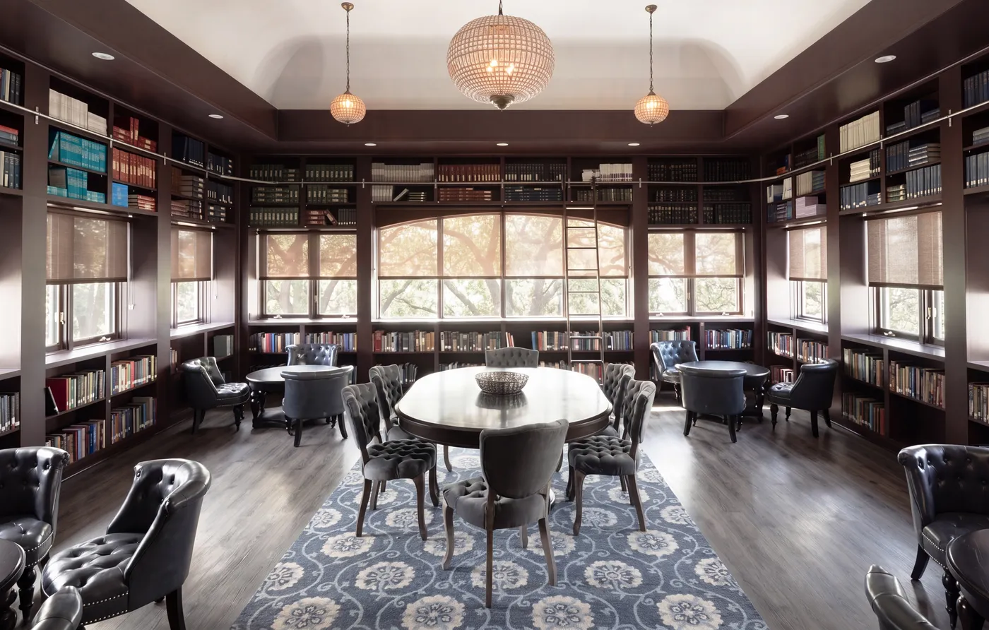 Interior library at The Lovett Center: floor-to-ceiling bookshelves on every wall, an oval table with tufted chairs at the center, pendant lights overhead.