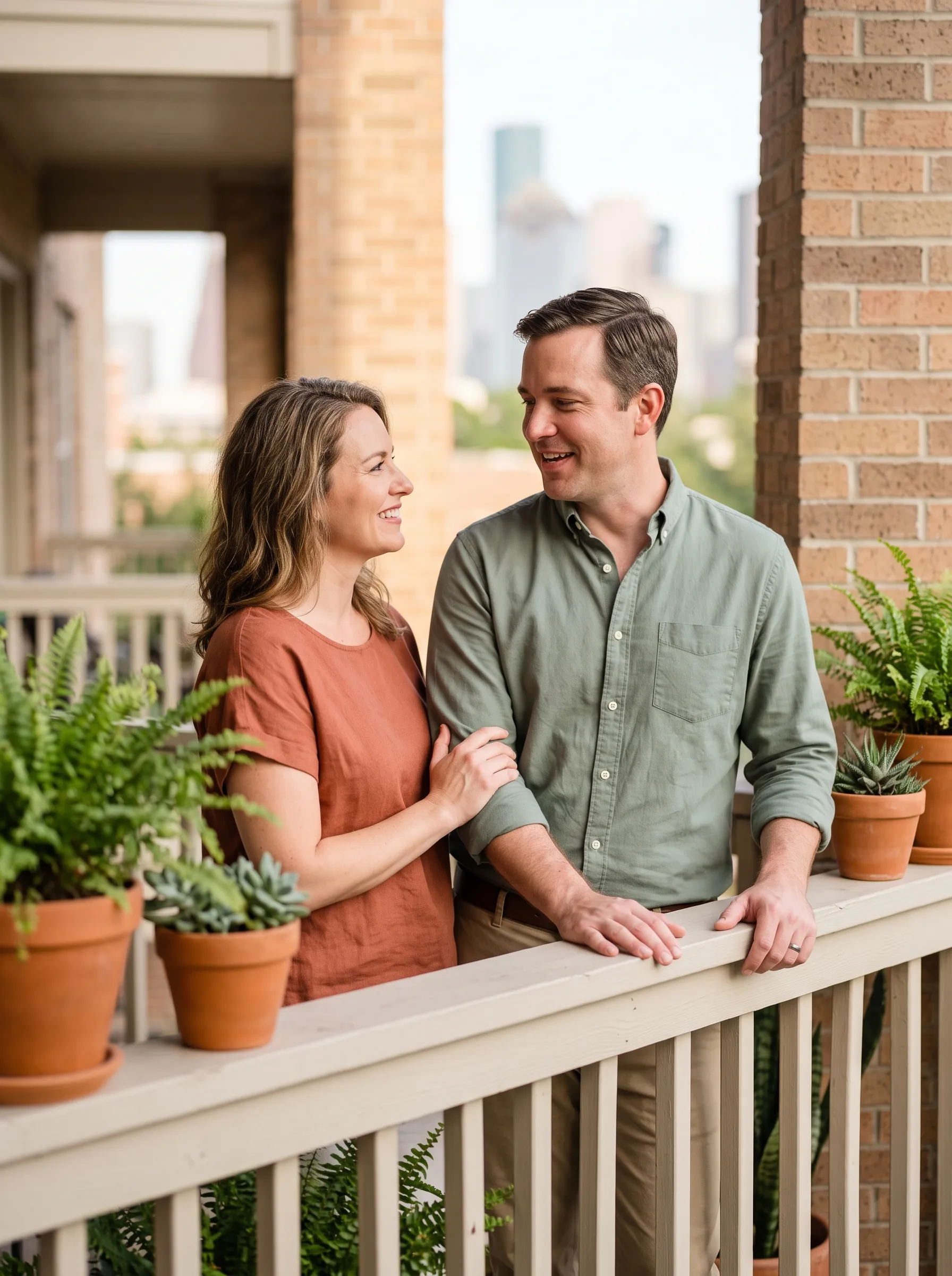 A warm, reconnected couple sharing a relaxed moment together on a sunlit Montrose balcony in Houston, with the downtown skyline soft in the late-afternoon light.