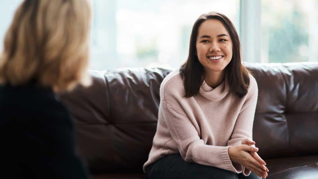 A woman seated on a couch and talking to a therapist at bipolar disorder treatment in Houston. 