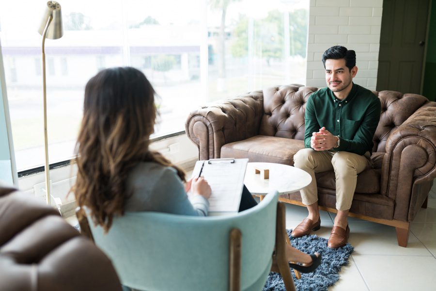 man sitting on a couch inquiring about the pros and cons of psychodynamic therapy